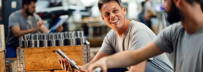 Two happy steel workers preparing manufacture products for the distribution and communicating in industrial facility. Focus is on mid adult worker.