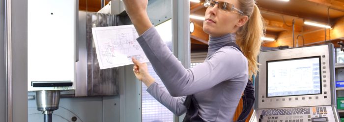 A young woman works as a computerized 
numerical control technician. She is seen at
her workplace wearing a blue overall.